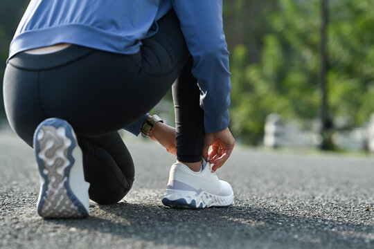 Cropped image of female runner tying shoelaces, getting ready for jogging outdoors. Fitness, sport and healthy lifestyle concept