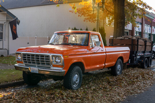 Orange Ford F250 custom Pickup with trailer loaded with firewood. 1979 retro Ford parked at the street side on sunny autumn day. Snohomish, WA, USA - October 2022
