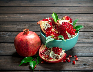 Pieces of ripe pomegranate in bowl and one ripe pomegranate with leaves.