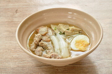 large rice noodles slice sausage with chop and crispy pork topping soft boiled egg in soup on bowl   