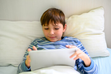 Smiling boy lying on his bed looking at a tablet