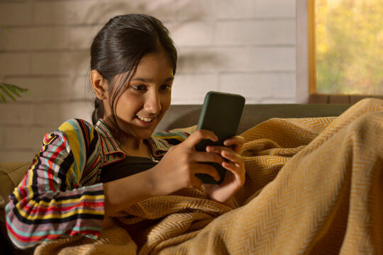 Girl using mobile phone while leaning on sofa in living room
