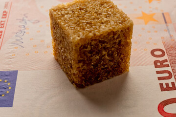 The image of a brown sugar cube resting on a Euro banknote, symbolizing the unequal distribution of resources during times of food crisis - 561203667