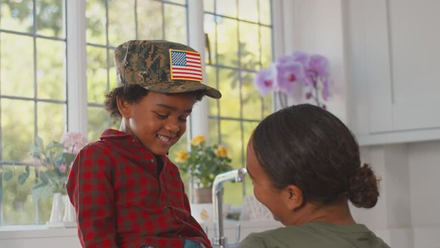 American Army Mother In Uniform Home On Leave Playing With Son Wearing Her Cap In Family Kitchen
