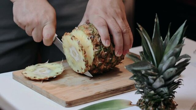 carving a pineapple on a board with a fruit salad knife