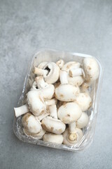Champignon mushrooms in the plastic box at the grey background	