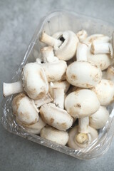 Champignon mushrooms in the plastic box at the grey background	