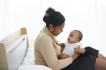 African young mother hugging and playing with her adorable baby on bed