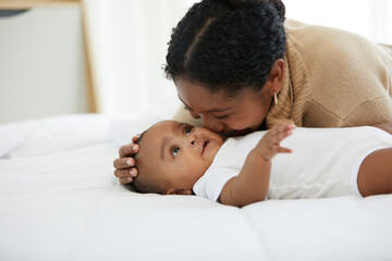 African young mother kissing her infant baby lying on the bed