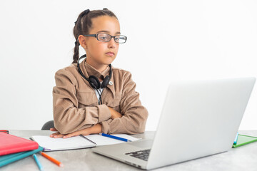 Portrait of little girl in wireless headset using laptop, studying online at home, interested happy student typing on keyboard looking at pc screen, watching webinar, online course, doing homework.