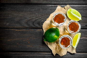 Tequila in a shot glass on paper with lime.