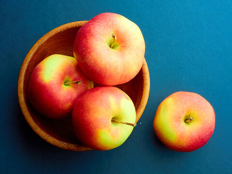 Ripe yellow-red apples in a wooden bowl on a blue background.