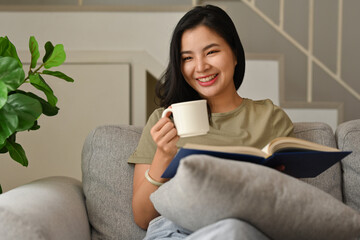 Domestic life and leisure activity lifestyle with Millennial Asian woman enjoy reading book and morning coffee in hand.