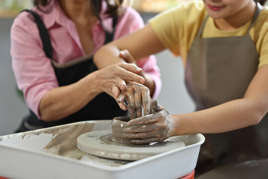 Close up and cropped image with Senior artisan teaching Young student using hand to sculpt a pot clay.