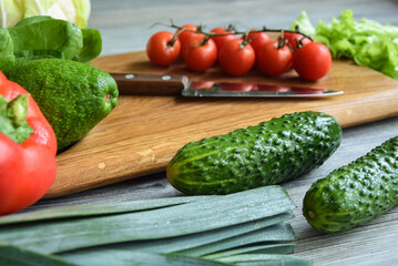 Closeup fresh organic vegetables with kitchen knife on cutting board wooden table indoors. Group of red green food ingredients for cooking healthy vegetarian eating at home. Preparing green salad