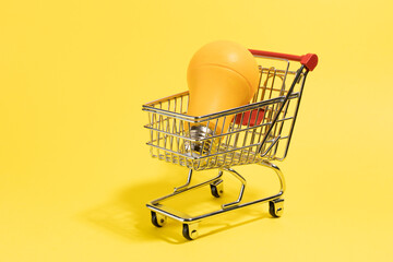 Shoping cart with light bulb on yellow background. Copy, empty space for text energy price concept