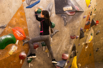Little girl free climbing on artificial wall in gym, bouldering
