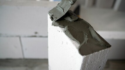 A bricklayer makes a concrete wall from a cement block and plaster at a construction site. The adhesive solution is applied to the floor. 
