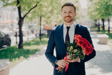 Smiling stylish stubbly gentleman in dark blue tuxedo with big bouquet