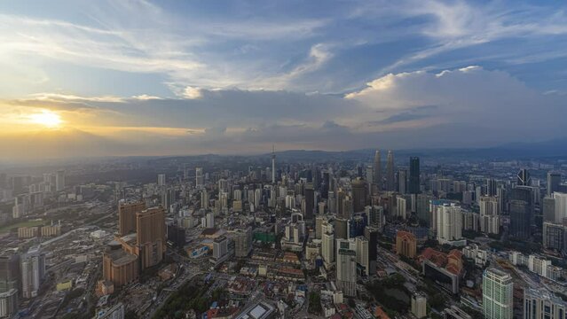 Aerial day-time time lapse overlooking a wide view of a city skyline with dancing rays before sunset in Kuala Lumpur, Malaysia. Tilt down motion timelapse.