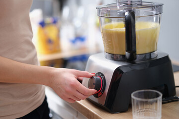 Woman is making smoothie or mixing dough in electric blender