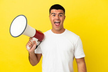 Young handsome man over isolated yellow background holding a megaphone and with surprise expression - obrazy, fototapety, plakaty