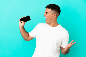 Young handsome man over isolated blue background using mobile phone and singing