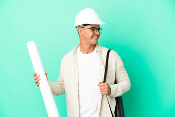 Young architect man holding blueprints over isolated background looking side