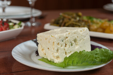 Big white piece of asian Korean tofu soy cheese on wooden board with greens