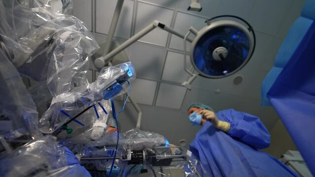 Robotic arms of surgery equipment working at operation. Nurse and surgeon collaborate with modern equipment. Low angle view.