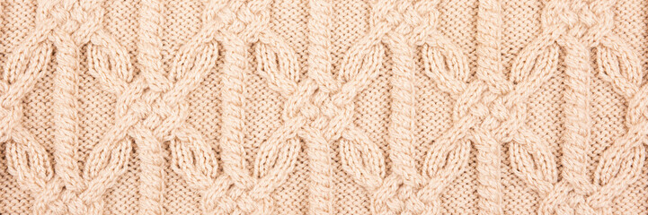 Knitted beige background. Large knitted fabric with a pattern. Close-up of a knitted blanket. Horizontal ornament. Banner