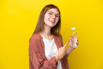 Young English woman with a bottle of water isolated on yellow background pointing back