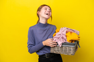 Young English woman holding a clothes basket isolated on yellow background laughing