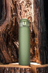 Promotional photo of the bottle. Photo of a thermos. Thermos of olive color against the background of tree bark. - obrazy, fototapety, plakaty