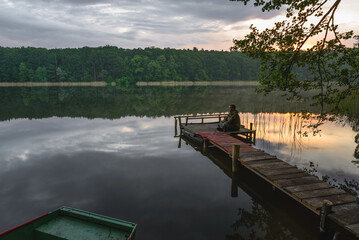 man sitting on a bridge during sunrise at the lake - 561218455