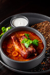 Solyanka soup with meat, sausage, vegetables, olives and lemon in bowl on wooden table background