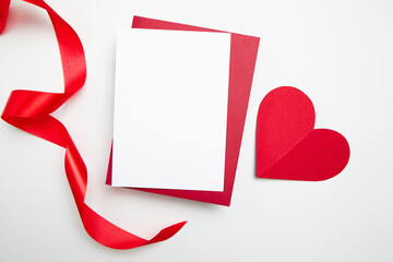 Valentine Day card mockup with red heart and ribbon on white background, top view, flat lay. Blank invitation, flyer, greeting card and envelop with holiday decor. Empty love letter