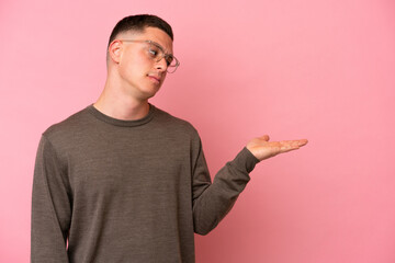 Young Brazilian man isolated on pink background holding copyspace with doubts