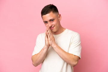 Young Brazilian man isolated on pink background keeps palm together. Person asks for something
