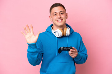 Young brazilian man playing with a video game controller isolated on pink background counting five with fingers