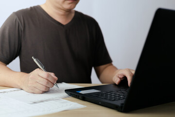 Fototapeta premium Man using laptop computer and taking notes in planning. which is payment online, sits on the chair in the living room at home on a laptop. The concept of finance and online shopping.