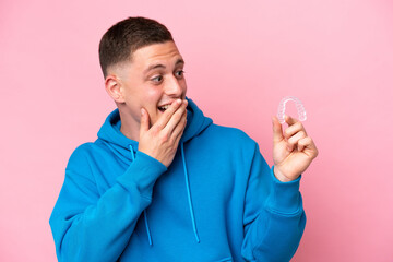 Young Brazilian man holding invisible braces isolated on pink background with surprise and shocked facial expression