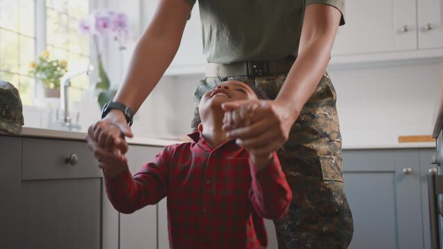 American Army Mother In Uniform Home On Leave Playing With Son In Family Kitchen