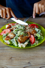 Woman eating salad with grilled chicken breast with vegetables and herbs . Caesar salad