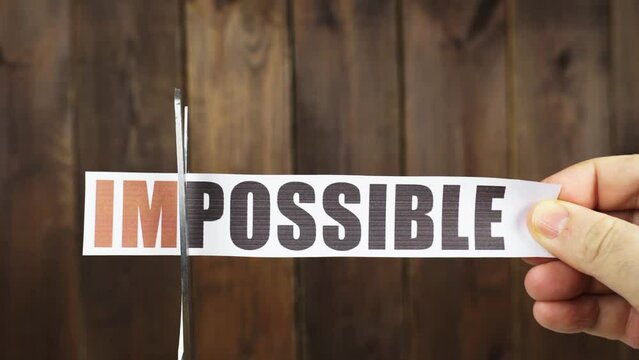 A man cuts with scissors a strip of paper with the inscription - IMPOSSIBLE.