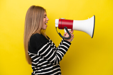 Young caucasian woman isolated on yellow background shouting through a megaphone to announce something in lateral position