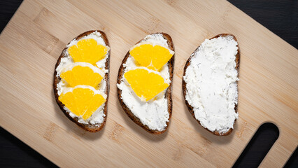 Toasts with cottage cheese and orange on a cutting board
