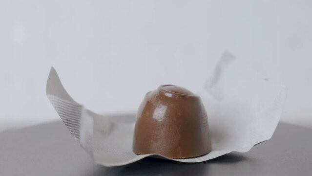 A chocolate candy on a foil wrapper lies on a turntable and spins. Close-up.