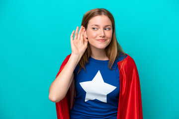 Super Hero caucasian woman isolated on blue background listening to something by putting hand on...