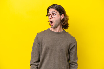 Fototapeta premium Caucasian handsome man isolated on yellow background doing surprise gesture while looking to the side